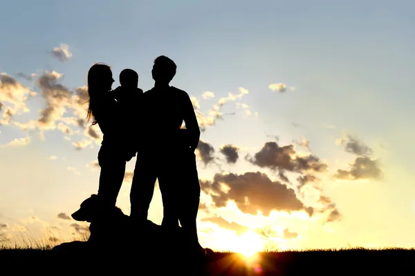 Jovem família feliz e silhueta de cachorro no pôr do sol — Fotografia de Stock