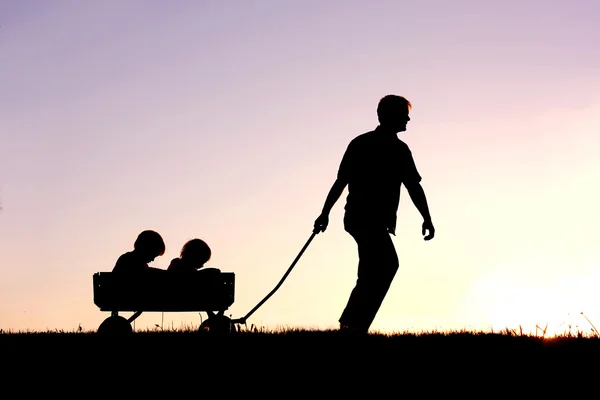 Silhueta do Pai Puxando Filhos em Vagão ao pôr do sol — Fotografia de Stock