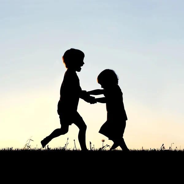 Silueta de niños pequeños y felices bailando al atardecer —  Fotos de Stock