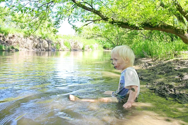 Niño sentado en el río Muddy en el bosque — Foto de Stock