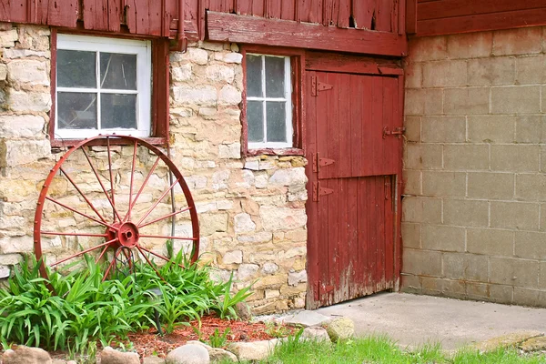 古色古香的车轮，倚在老石头谷仓的墙上 — 图库照片