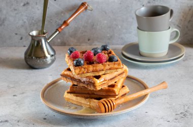 Böğürtlenli waffle, bal, jezva ve açık beton arka planda fincanlar.