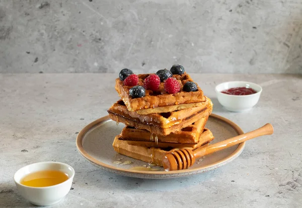 Böğürtlenli waffle, bal ve beton arka planda tahta kaşık.
