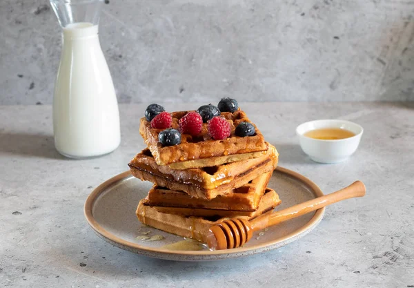 Böğürtlenli waffle, bal ve açık beton arka planda bir şişe süt
