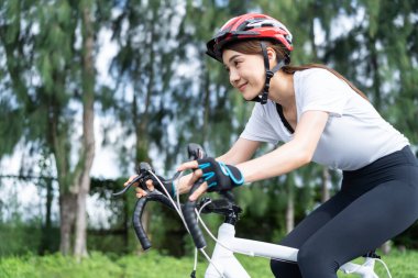 Akşam vakti parkta bisiklete binen Asyalı genç bayan. Spor giyimli, formda, kasklı, sporcu kıyafetli güzel bir sporcu. Spor kaskı takıyor, spor yapıyor, sağlık durumu ve tazeliği için bisiklet egzersizi yapıyor..