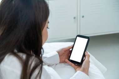 Asyalı bir kadın evdeki beyaz ekranla çevrimiçi video görüşmesinde konuşuyor. Pijamalı çekici bir kız, sabah yatak odasında uyandıktan sonra sanal bir uzaktan kumandada cep telefonuyla konuşmayı sever..