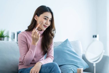 Asyalı profesyonel kadın sanatçı evde kalıp makyajın keyfini çıkarıyor. Çekici, güzel bir kız kanepeye oturur, mutlu bir şekilde aynaya bakar ve yüzünü boyayan kaşlarla evin güzelliğinin tadını çıkarır..