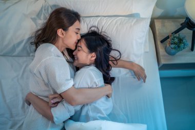 Asyalı güzel lezbiyen çift yatağa uzanıp birbirlerine sarılıyorlar. Pijamalı çekici romantik kız arkadaş geceyi yatak odasında, evde birlikte geçiriyor. Homoseksüel-LGBTQ kavramı