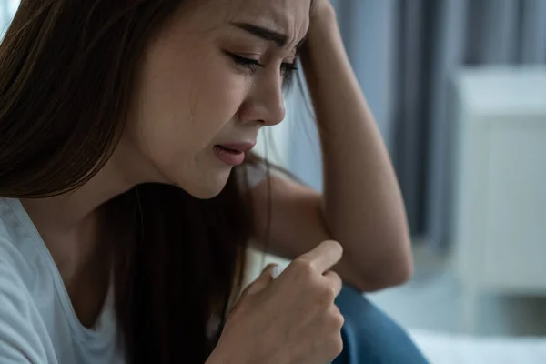 Asyalı güzel depresyonlu kız gözyaşları içinde yatakta oturuyor. Çekici, mutsuz genç bir kadın üzgün, yalnız ve hayat probleminden dolayı üzgün ve evdeki karanlık gece odasında elinde mendil tutuyor.