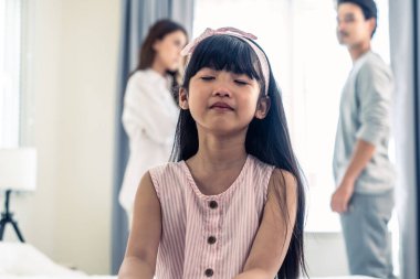 Ebeveynler kavga ederken ya da kavga ederken Asyalı küçük kız ağlıyor. Küçük bir kız çocuğu gözyaşları içinde kalbi kırık bir şekilde yatakta oturuyor ve evde şiddet görmek istemiyor. Aile sorunları ayrılığı kavramı