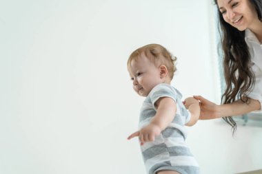 Beyaz tenli, tatlı, küçük erkek bebek, annesiyle evde yürümeyi öğreniyor. Mutlu bir aile, annesi küçük çocuğuna destek oluyor. Evde oturma odasında yeteneğini geliştirmek için babasıyla ilk adımını atıyor..