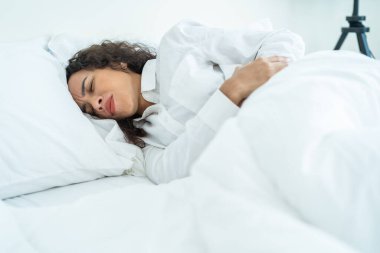 Pijamalı güzel hasta Latin kız yatak odasından kalkıyor. Çekici genç bir kadın yatakta uyandıktan sonra kötü ve acı verici hisseder. Karın ağrısı ya da regl geçirdikten sonra sabah karnını sıkar..