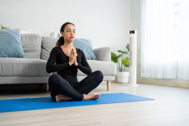 Latin genç ve aktif bir kadın evde Yoga pilates yapıyor. Spor giyim sektöründeki çekici kız kendini mutlu hisset ve rahatla. Oturma odasındaki çevrimiçi eğitmenin alıştırma videosunu izle.