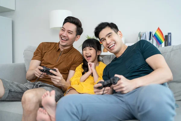 亚洲男同性恋家庭和年幼的女儿一起在家里玩游戏 小女儿坐在沙发上 与迷人的浪漫的男性小两口儿在家里玩操纵杆游戏 男女同性恋 双性恋 变性者和变性者问题概念 — 图库照片