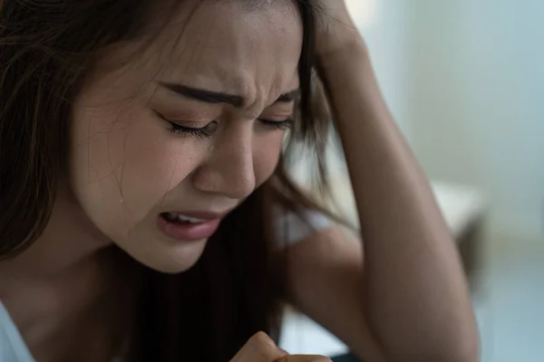Asyalı güzel depresyonlu kız gözyaşları içinde yatakta oturuyor. Çekici, mutsuz genç bir kadın üzgün, yalnız ve hayat probleminden dolayı üzgün ve evdeki karanlık gece odasında elinde mendil tutuyor.
