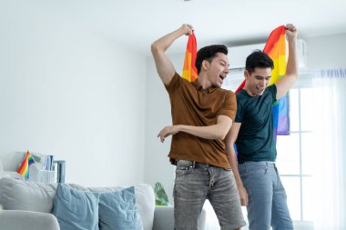 Asyalı yakışıklı eşcinsel aile LGBTQ bayrağı taşıyor ve birlikte dans ediyorlar. Çekici romantik erkek lgbt çifti müzik dinleyerek ve eğlenerek, neşeli gururla eğlenerek ve gökkuşağı bayrağı taşıyarak vakit geçirir..