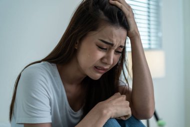 Asyalı güzel depresyonlu kız gözyaşları içinde yatakta oturuyor. Çekici, mutsuz genç bir kadın üzgün, yalnız ve hayat probleminden dolayı üzgün ve evdeki karanlık gece odasında elinde mendil tutuyor.