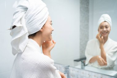 Asyalı güzel kadın yüz bakımı için yumuşak ve cilt bakımı yapıyor. Çekici kadın dokunuşları ve gençleşme için krem sürme duştan sonra nazikçe. Güzellik, cilt bakımı ve sağlık