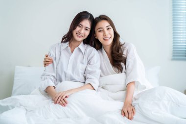 Asyalı güzel lezbiyen çiftin portresi sarılıyor ve kameraya bakıyor. Pijamalı çekici romantik kız arkadaş sabahları yatak odasında birlikte vakit geçiriyorlar. Homoseksüel-LGBTQ kavramı.