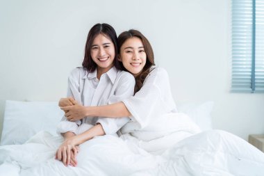 Asyalı güzel lezbiyen çiftin portresi sarılıyor ve kameraya bakıyor. Pijamalı çekici romantik kız arkadaş sabahları yatak odasında birlikte vakit geçiriyorlar. Homoseksüel-LGBTQ kavramı.