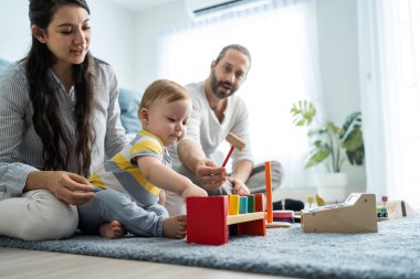 Beyaz, mutlu bir ebeveyn, bebek bebekle oturma odasında oynuyor. Çekici bir çift anne ve baba, küçük bir çocuğun gelişimine bakıyor. Evde etkinlik ilişkisi.