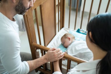 Beyaz aileler evdeki yatak odasında uyuyan bebekle ilgileniyorlar. Çekici mutlu aile çifti, anne ve baba battaniyeyi üzerine örterler rahat bir şekilde uykuya dalarlar küçük çocuğu sabah yatağında kestirirler.