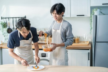 Asyalı genç LGBTQ erkek eşcinsel aile evde mutfakta yemek pişirmeyi seviyor. Çekici, romantik erkek çift önlük giyer. Evde spagetti yaparken mutlu ve neşeli hissederler.