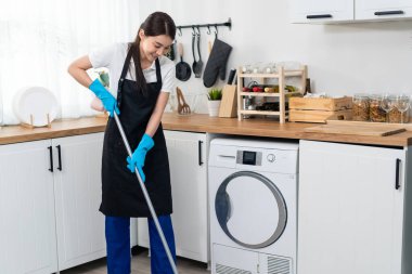Asian active cleaning service woman worker cleaning in kitchen at home. Beautiful young girl housekeeper cleaner feel happy and mopping on floor working for housekeeping housework or chores in house.