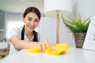 Asian cleaning service woman worker cleaning in living room at home. Beautiful girl housewife housekeeper cleaner feel happy and wiping messy dirty working table for housekeeping housework or chores.