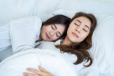 Asian beautiful lesbian couple lying down on bed and hug each other. Attractive romantic lgbt woman gay in pajamas sleeping in early morning time together in bedroom at home. Homosexual-LGBTQ concept.