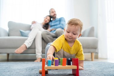 Caucasian loving parent looking at baby toddler playing in living room. Attractive couple mother and father watch young little infant son child's development. Activity relationship at home in house.