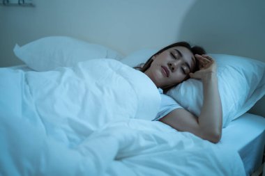 Asian beautiful woman lying down on bed in bedroom, dreaming at night. Attractive young female in pajamas sleeping alone on comfortable pillow and cozy blanket in dark room for health care at home.