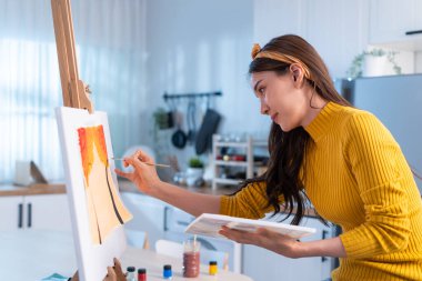 Asian young talented woman artist coloring on painting board in house. Attractive beautiful female draw art picture, creating artwork with watercolor paint and brush enjoy creativity activity at home.