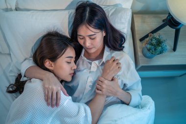 Asian beautiful lesbian couple lying down on bed and hugging each other. Attractive romantic girl friend in pajamas spending night leisure time together in bedroom in house.