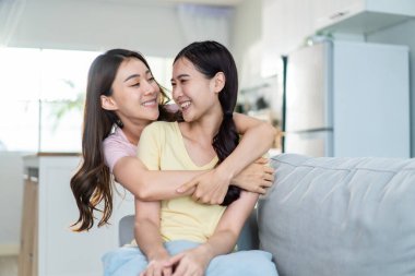 Asian beautiful lesbian women couple hugging girlfriend in living room. Attractive two female gay friend sitting on sofa in living room, feel happy and enjoy spending time together on holiday in house