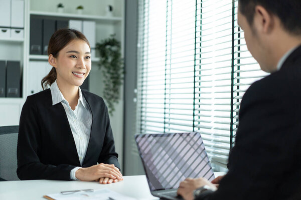 Asian beautiful woman talk with hr manager for job interview in office. Attractive female sit on table and give resume to human resources managers business recruit people for apply job at workplace.