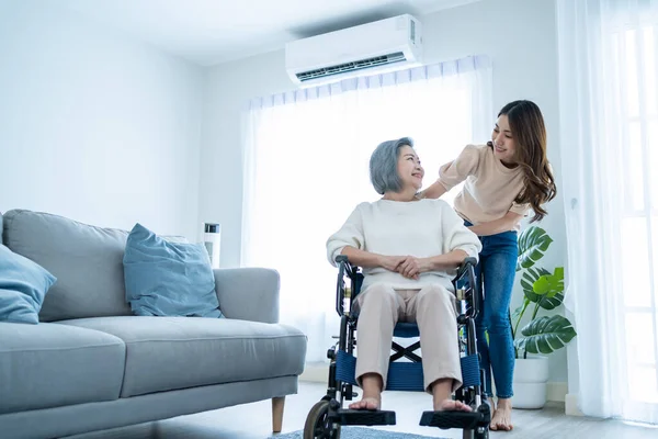 Asyalı genç kız evde tekerlekli sandalyeli yaşlı kadını destekliyor. Güzel bir kız yaşlı, olgun, engelli bir anneye yardım ediyor ve onunla ilgileniyor. Oturma odasında fizik tedavi görüyor.