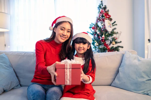 Küçük Asyalı kızın portresi. Annemden hediye paketi açık. Mutlu aile, küçük çocuk mutlu ve sürpriz için heyecanlı. Anneler Noel 'i birlikte kutlamaya ve kameraya bakmaya hazır..