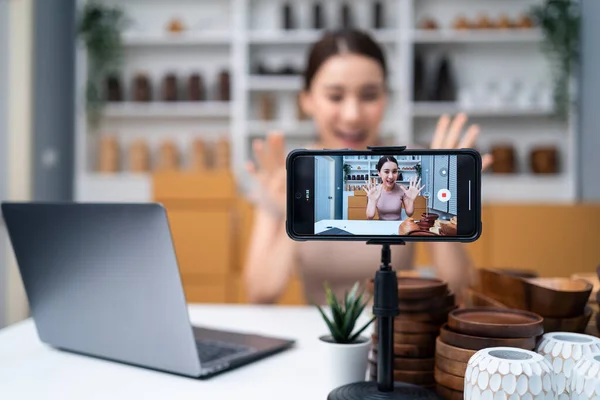 Asian beautiful woman sell vase product online live streaming at home. Young attractive girl use laptop computer shows goods to customer and present detail. Remote buying and purchase shopping concept