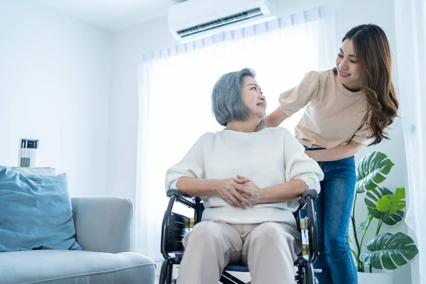 Asyalı genç kız evde tekerlekli sandalyeli yaşlı kadını destekliyor. Güzel bir kız yaşlı, olgun, engelli bir anneye yardım ediyor ve onunla ilgileniyor. Oturma odasında fizik tedavi görüyor.