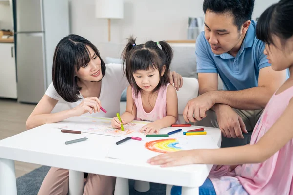 Asian young kid daughter coloring and painting on paper with parents. Happy family activity, Little girl children learn how to draw art picture enjoy creativity with mother and father in living room.
