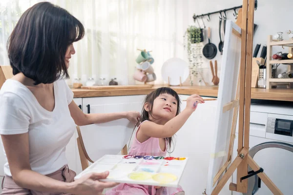 Asian young happy kid daughter coloring on painting board with mother. Happy family activity, Little girl child learn how to draw art picture with watercolor paint and brush enjoy creativity with mom.