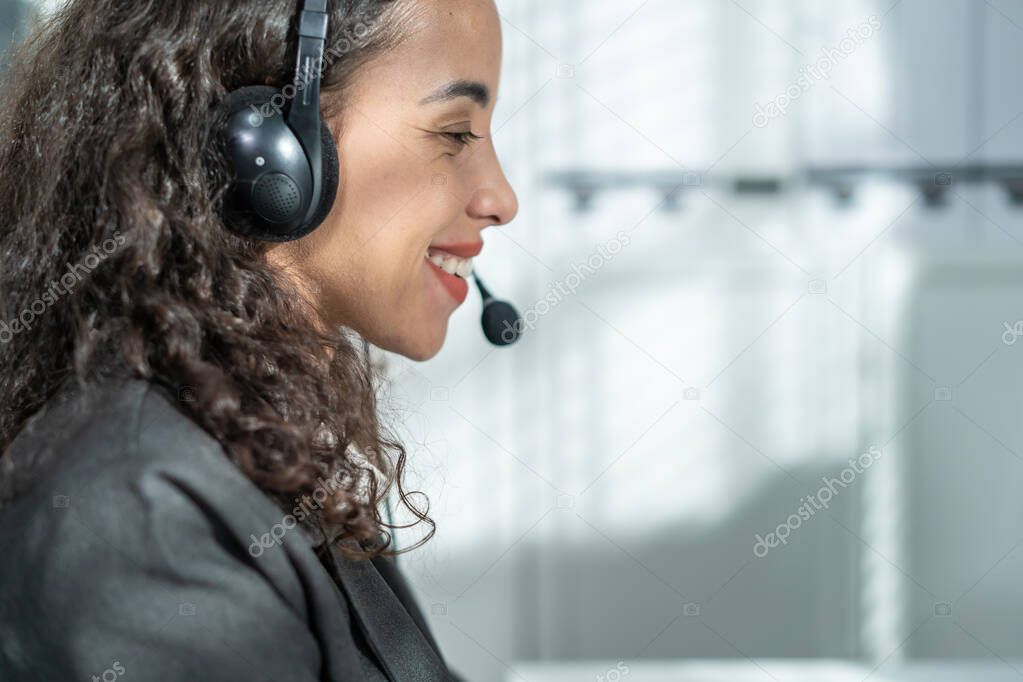 Latino beautiful business woman call center smile while work in office. Attractive young female employee worker in formal wear sit on table at workplace, use laptop computer talk to support customer.