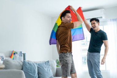 Asyalı yakışıklı eşcinsel aile LGBTQ bayrağı taşıyor ve birlikte dans ediyorlar. Çekici romantik erkek lgbt çifti müzik dinleyerek ve eğlenerek, neşeli gururla eğlenerek ve gökkuşağı bayrağı taşıyarak vakit geçirir..