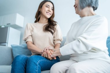 Asian lovely family, young daughter hugging and sit with older mother. Attractive woman granddaughter visit senior elder mature mom in house enjoy spend leisure time together in living room and smile.