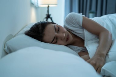 Asian beautiful woman lying down on bed in bedroom, dreaming at night. Attractive young female in pajamas sleeping alone on comfortable pillow and cozy blanket in dark room for health care at home.