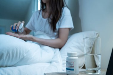 Asian unhappy sick girl in pajamas take medicine before sleep on bed. Attractive beautiful young woman feel frustrated to take many drug to in dark night in bedroom at home. Healthcare-medical concept