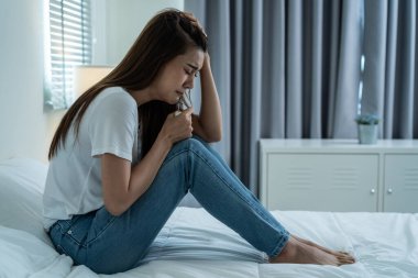 Asyalı güzel depresyonlu kız gözyaşları içinde yatakta oturuyor. Çekici, mutsuz genç bir kadın üzgün, yalnız ve hayat probleminden dolayı üzgün ve evdeki karanlık gece odasında elinde mendil tutuyor.