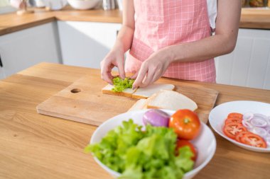Close up of attractive woman making sandwich for breakfast in morning. Beautiful girl wear apron enjoy eat clean vegetables healthy food for health care in house. Diet lose weight and foods concept.