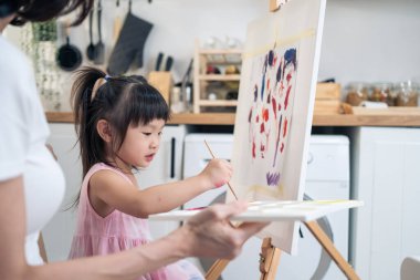 Asian young happy kid daughter coloring on painting board with mother. Happy family activity, Little girl child learn how to draw art picture with watercolor paint and brush enjoy creativity with mom.